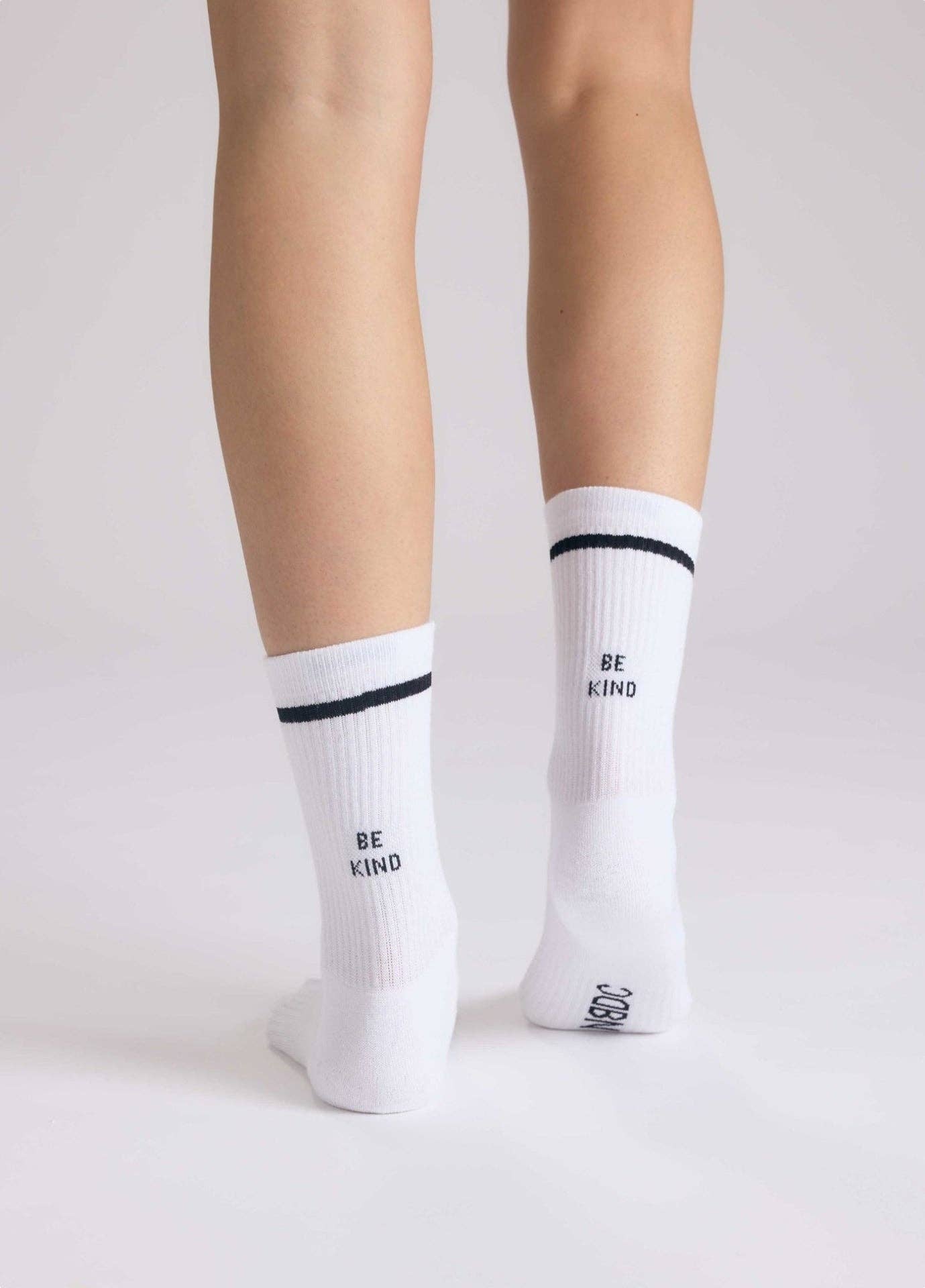 BE KIND Statement Socken von NBDC in Weiß mit schwarzem Schriftzug getragen – Nohna