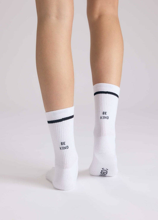 BE KIND Statement Socken von NBDC in Weiß mit schwarzem Schriftzug getragen – Nohna