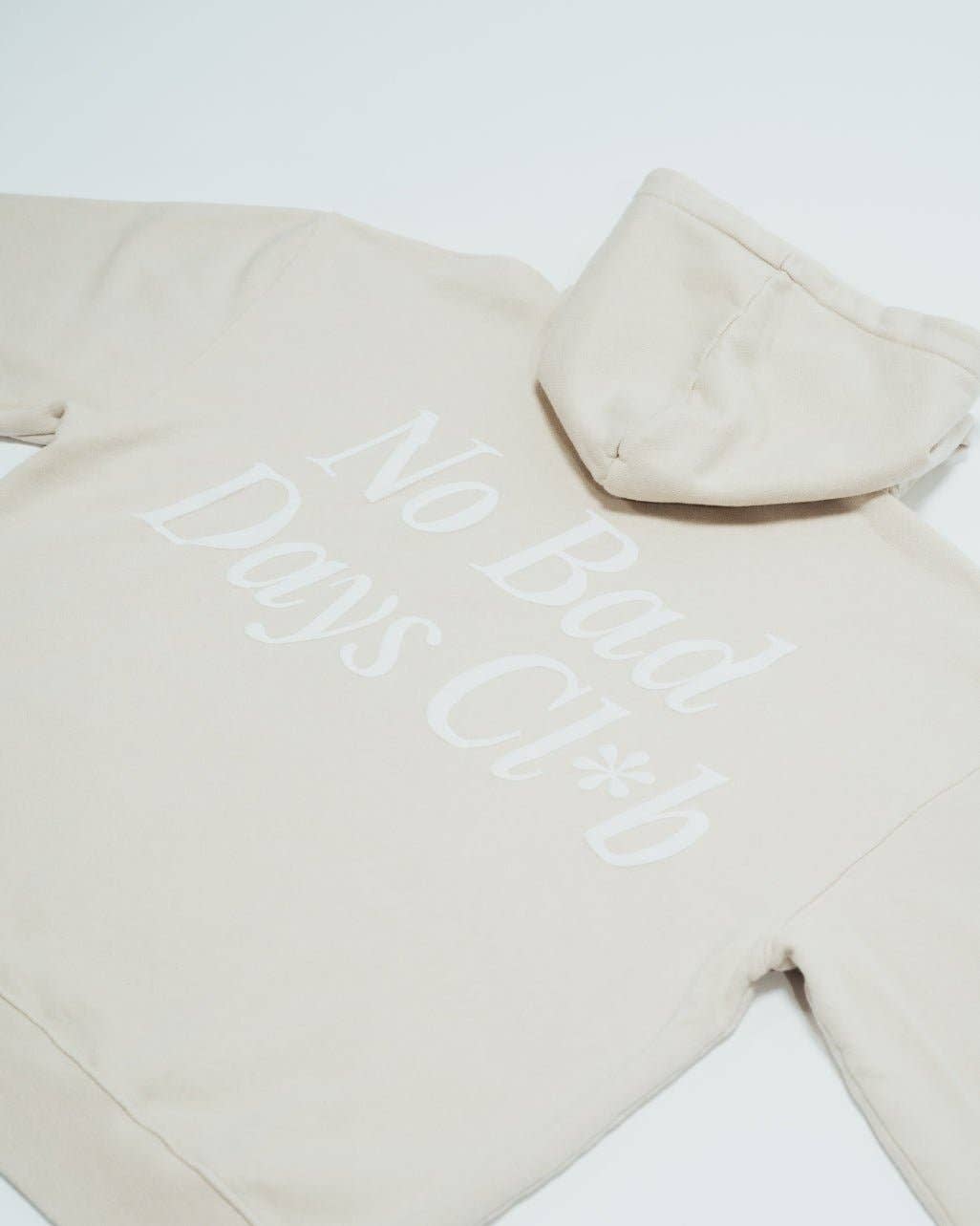 No Bad Days Club Hoodie in Sandbeige mit weißem Backprint – Rückenansicht liegend, Nohna