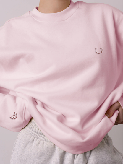 Croissant Sweatshirt Unisex in hellem Rosa mit Smiley-Print und Croissant-Stickerei am Ärmel – Nohna